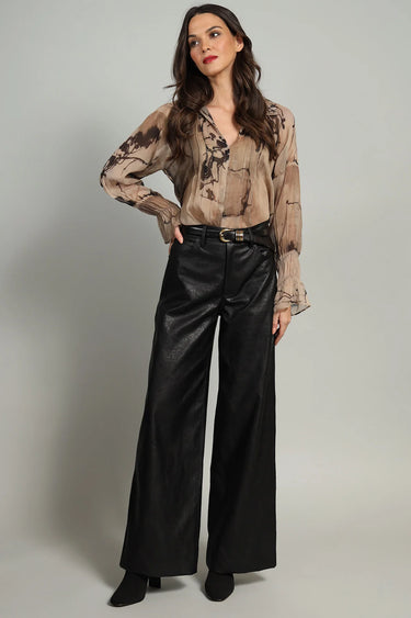 A woman wearing a chiffon printed brown blouse and black pants on a white background.