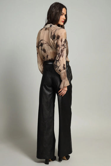 A woman facing backwards wearing a chiffon printed brown blouse and black pants on a white background.