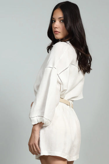 Woman wearing a white outfit with a belt on a gray background