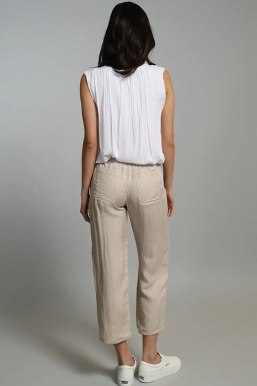 A woman wearing cropped linen beige pants and a white top on a neutral background 