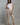 A woman wearing cropped linen beige pants and a white top on a neutral background 