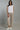 A woman wearing cropped linen beige pants and a white top on a neutral background 
