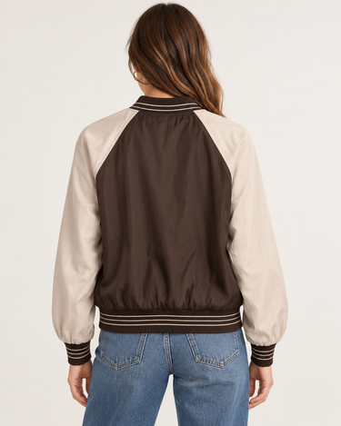a woman wearing a reversible baseball Brown jacket with black jeans on a neutral background.