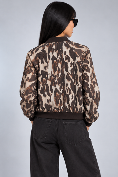 a woman wearing a reversible baseball leopard jacket with black jeans on a neutral background.