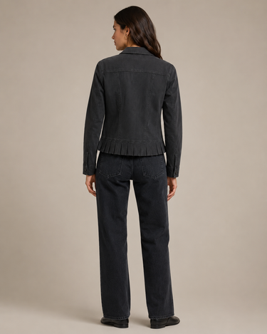 A woman shown from the back wearing a dark charcoal gray fringed denim jacket and matching dark denim jeans against a solid beige studio background.