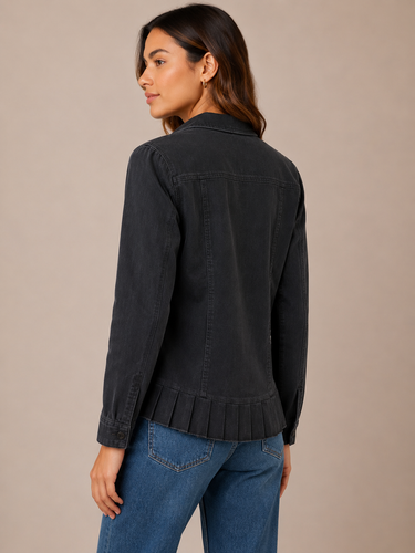 A woman wearing a dark charcoal gray denim jacket with a pleated hem, shown from a three-quarters back view against a solid beige studio background.