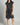 Woman wearing a black sleeveless dress with buttons on a gray background