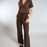A woman wearing a brown top and satin drawstring brown pants on a white background 