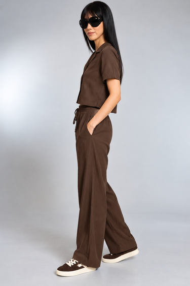 A woman wearing a brown top and satin drawstring brown pants on a white background 