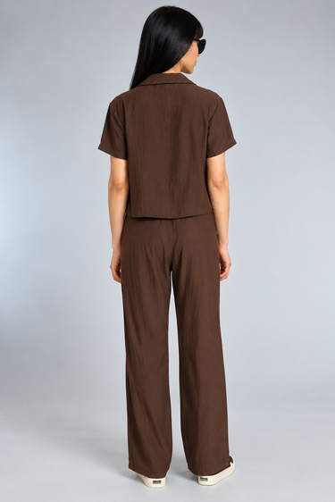 A woman wearing a brown top and satin drawstring brown pants on a white background 