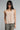 A woman wearing a beige satin tank with a split hem and grey trousers  on a studio background.