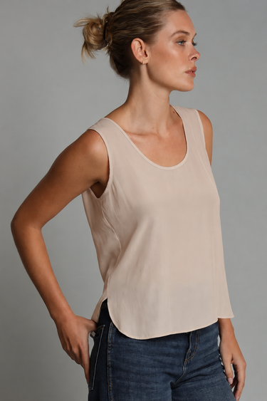 A woman wearing a beige satin tank with a split hem and blue jeans on a studio background.