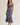 A woman modeling a blue floral satin slip dress with thin straps and a ruffled hem, standing against a plain light beige studio background.