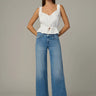Woman wearing a white peplum top and blue jeans on a gray background