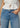 Person wearing a white blouse and blue jeans with a neutral background