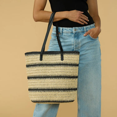 Person holding a striped woven bag against a beige background