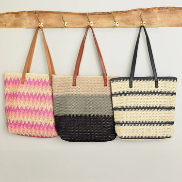 Three woven bags hanging on a wooden rack against a plain wall.