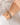 A close-up of a person's wrist wearing three beaded bracelets: one gold with a pink tassel charm, one silver with dark blue beads, and one silver with light blue beads, against a soft white fabric background.