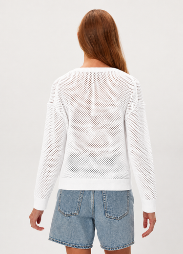 Woman wearing a white mesh sweater and denim shorts on a plain background
