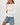Woman wearing a white knit sweater and denim shorts on a light gray background