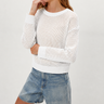 Woman wearing a white knit sweater and denim shorts on a light gray background