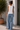 Woman wearing a white sleeveless top and light blue jeans standing outdoors.