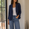 Woman wearing a navy blazer, white top, and blue jeans indoors.