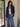 Woman wearing a navy blazer, white top, and blue jeans indoors.