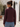 A woman wearing a long-sleeve cowl-neck jacket in deep burgundy, shown from the back. She is wearing blue jeans and standing in an outdoor courtyard with a white stucco wall, arches, and a potted olive tree in the background.