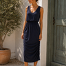 Woman wearing a navy blue dress standing outdoors next to a wooden door.