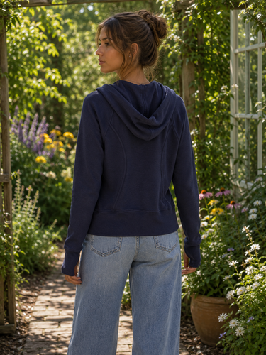 Woman wearing a navy hoodie and light blue jeans standing in a garden.