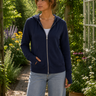 Woman wearing a navy blue hoodie and light blue jeans standing in a garden.