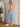 Woman wearing a white tank top and blue jeans standing in front of a mirror.