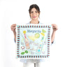 Woman holding a 'Margarita' themed tea towel with illustrations of a cocktail and ingredients.
