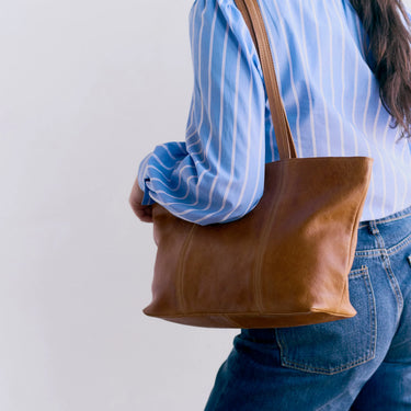 Person wearing a brown leather tote bag with a plain background