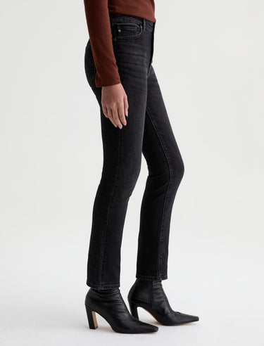 A woman standing sideways wearing slim straight jeans in black with black boots and a maroon long sleeve tee on a white background.