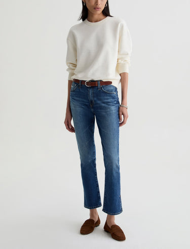 Person wearing a white sweater, blue jeans, and brown shoes on a white background