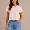 a woman wearing a crewneck cropped boxy fit tee in pale pink with jeans on a neutral background