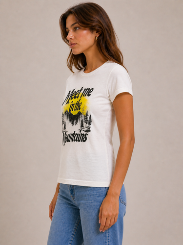 a woman wearing a white tee with “meet me in the mountians” written on the front
