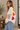 A woman wearing a beige v-neck cardigan with “LOVE” written in multi-colored letters at the middle of the sweater and hearts down the sleeve 