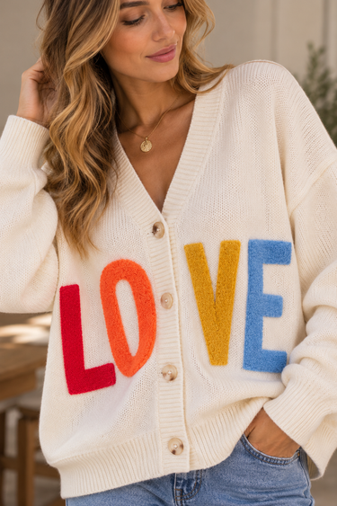 A woman wearing a beige v-neck cardigan with “LOVE” written in multi-colored letters at the middle of the sweater.