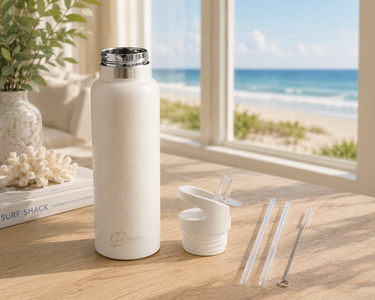 White reusable water bottle with accessories on a table with a beach view