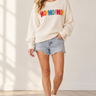 A woman wearing a white sweater with “HO!HO!HO!” written along the arms and shoulders in colorful letters.