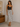 Woman wearing a black top and patterned skirt standing in a room with a wooden dresser and framed picture.