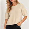 a woman wearing a knit short sleeve seater with gold sequins and black pants on a white background.