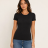 A woman modeling a fitted black short-sleeve crewneck t-shirt with blue jeans, standing against a plain off-white studio background.