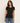 A woman modeling a fitted black short-sleeve crewneck t-shirt with blue jeans, standing against a plain off-white studio background.