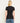 A woman viewed from the back wearing a fitted black short-sleeve crew-neck t-shirt and blue jeans, set against a plain off-white studio background.