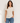 A woman modeling a short-sleeve crewneck t-shirt in a light cream color, paired with blue jeans, against a plain off-white background.