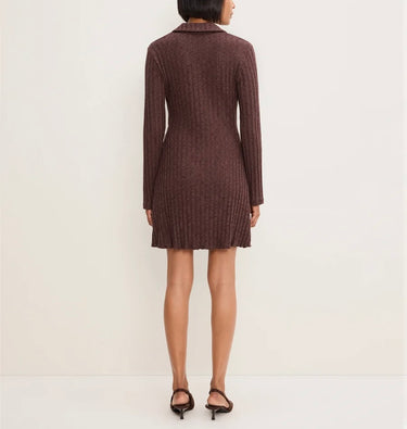 A woman viewed from the back wearing a dark brown ribbed knit long-sleeve mini dress with a collar, paired with black heeled sandals, against a plain off-white studio background.